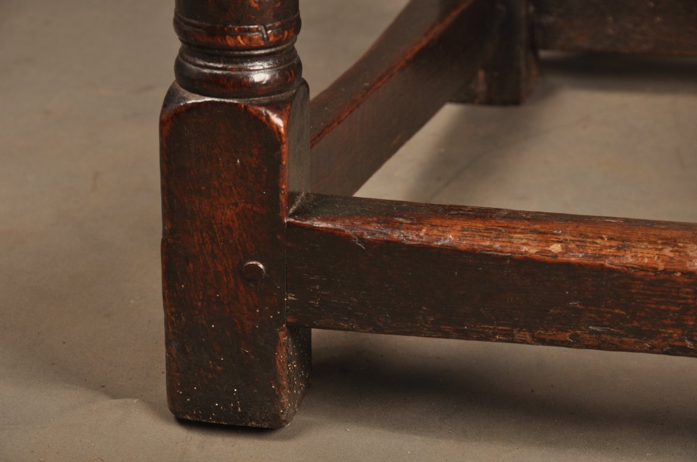 A 17th-century dark oak wainscot armchair featuring a carved lozenge back panel, turned front supports, and shaped armrests. View VII