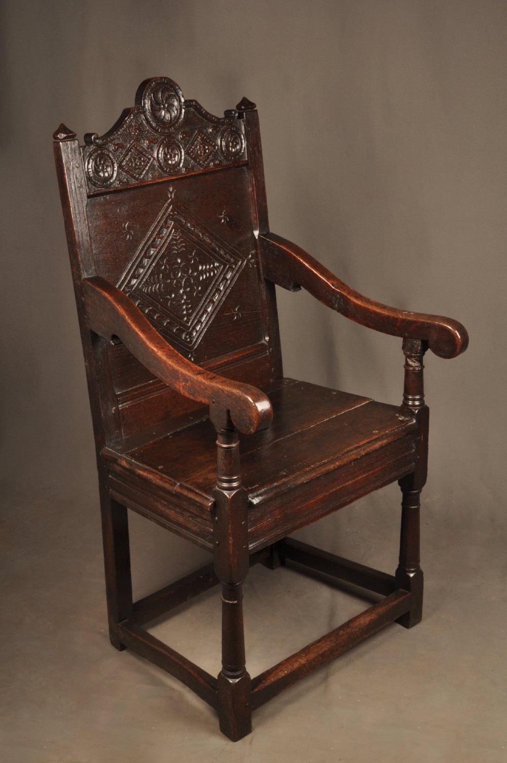 A 17th-century dark oak wainscot armchair featuring a carved lozenge back panel, turned front supports, and shaped armrests. View VIII