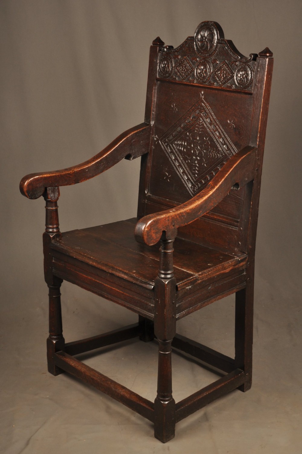 A 17th-century dark oak wainscot armchair featuring a carved lozenge back panel, turned front supports, and shaped armrests. View IX