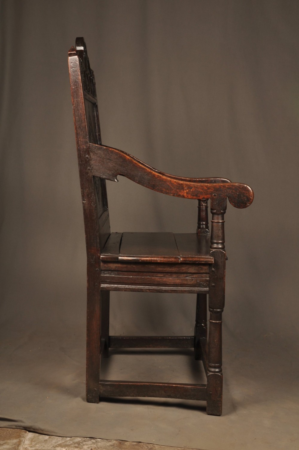 A 17th-century dark oak wainscot armchair featuring a carved lozenge back panel, turned front supports, and shaped armrests. View XII