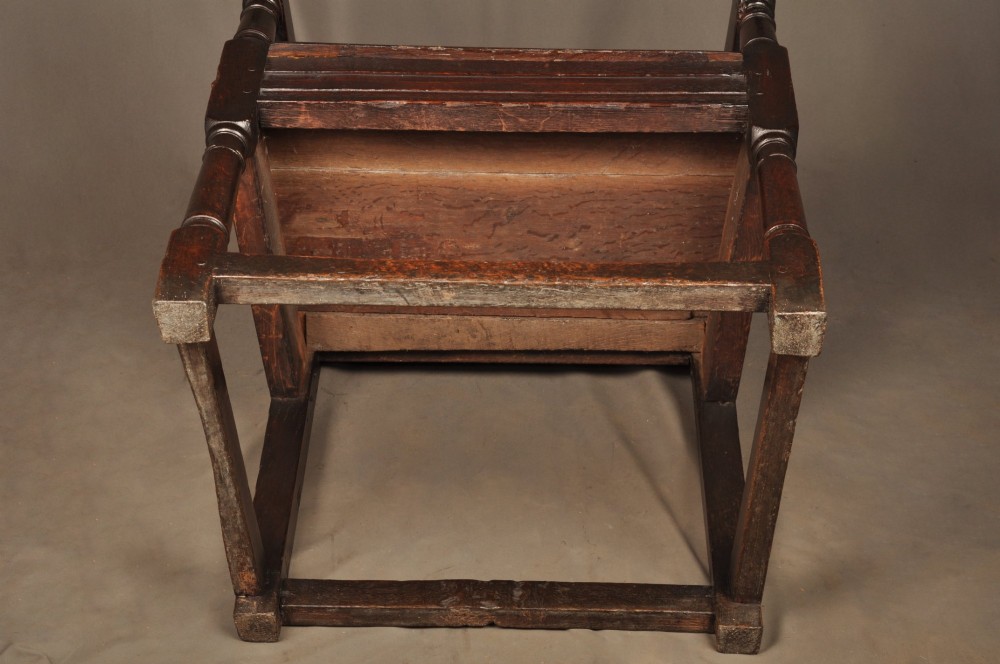 A 17th-century dark oak wainscot armchair featuring a carved lozenge back panel, turned front supports, and shaped armrests. View XIII