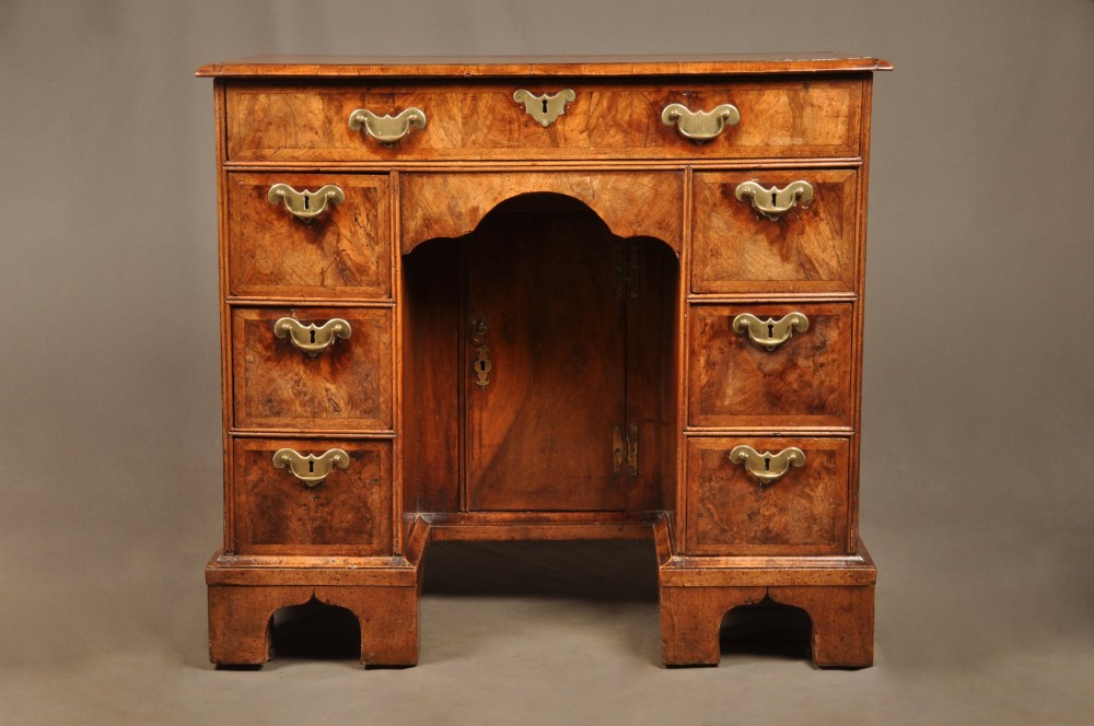 A Queen Anne walnut kneehole desk featuring figured wood veneers, seven drawers with brass handles, a central recessed cupboard, and bracket feet. View II