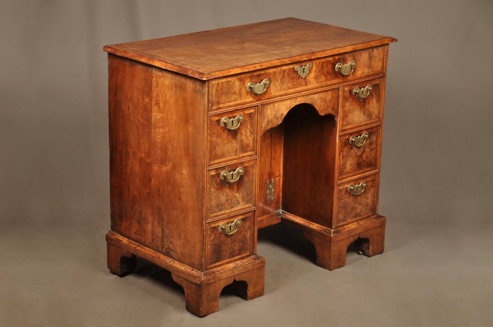 A Queen Anne walnut kneehole desk featuring figured wood veneers, seven drawers with brass handles, a central recessed cupboard, and bracket feet. View IV