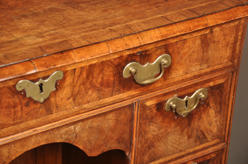 A Queen Anne walnut kneehole desk featuring figured wood veneers, seven drawers with brass handles, a central recessed cupboard, and bracket feet. View VII