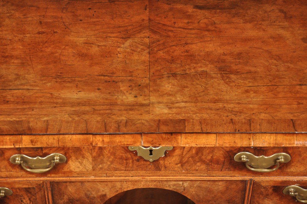 A Queen Anne walnut kneehole desk featuring figured wood veneers, seven drawers with brass handles, a central recessed cupboard, and bracket feet. View VIII