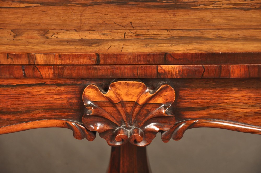 A Regency period rosewood fold-over card table featuring a carved apron, a central pedestal column, and a fluted quadripartite base on brass castors. View II