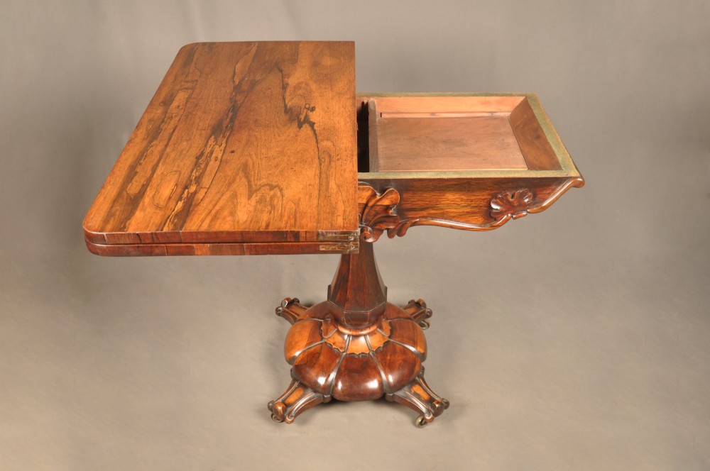 A Regency period rosewood fold-over card table featuring a carved apron, a central pedestal column, and a fluted quadripartite base on brass castors. View VII