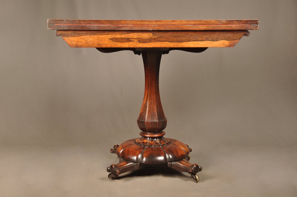 A Regency period rosewood fold-over card table featuring a carved apron, a central pedestal column, and a fluted quadripartite base on brass castors. View VIII
