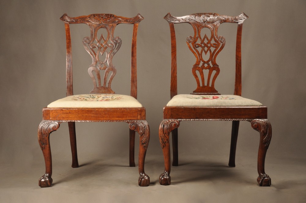 A pair of 18th-century George II mahogany side chairs featuring pierced carved splats, cabriole legs with claw and ball feet, and floral needlepoint drop-in seats.