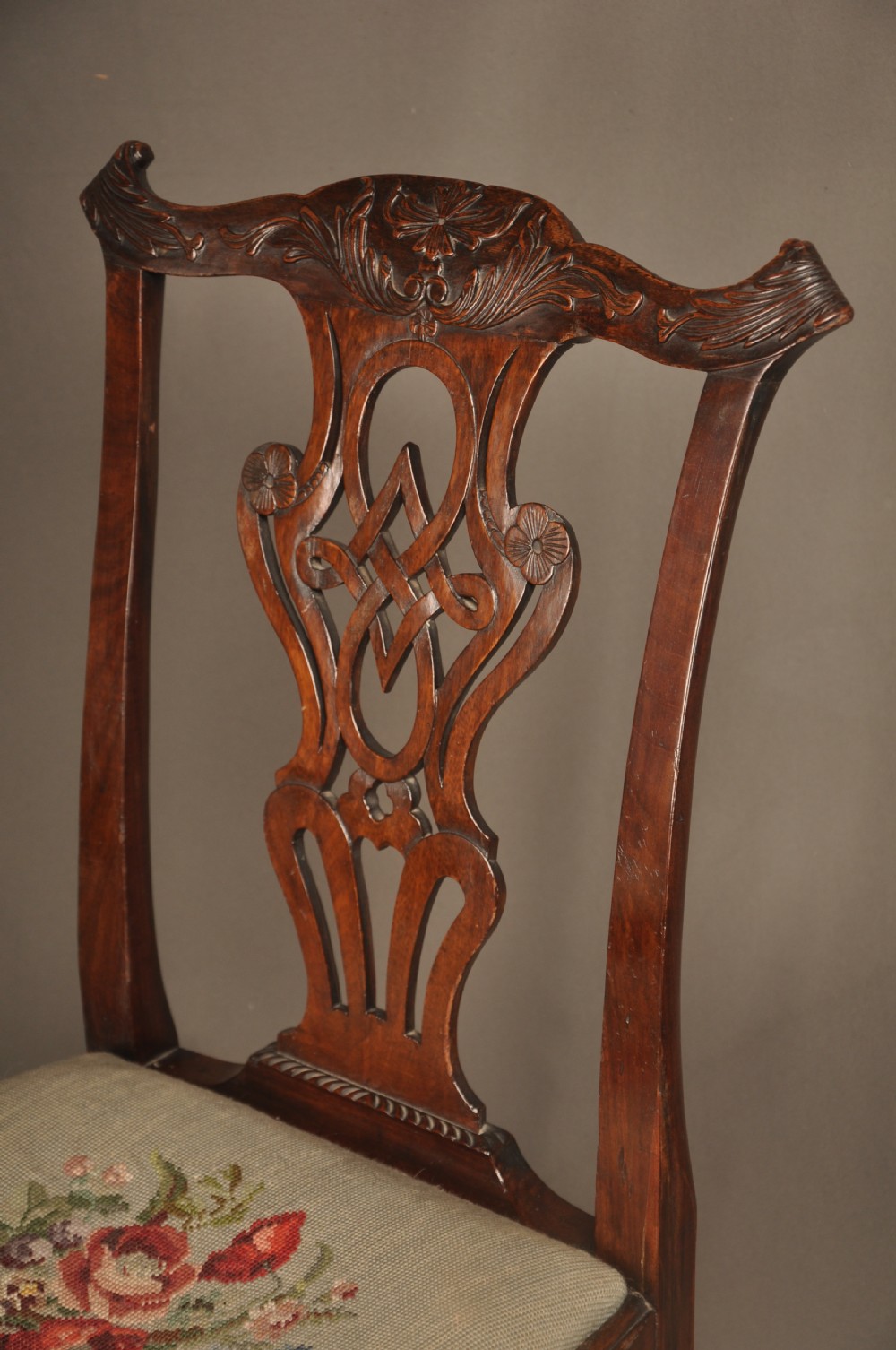 A pair of 18th-century George II mahogany side chairs featuring pierced carved splats, cabriole legs with claw and ball feet, and floral needlepoint drop-in seats. View V