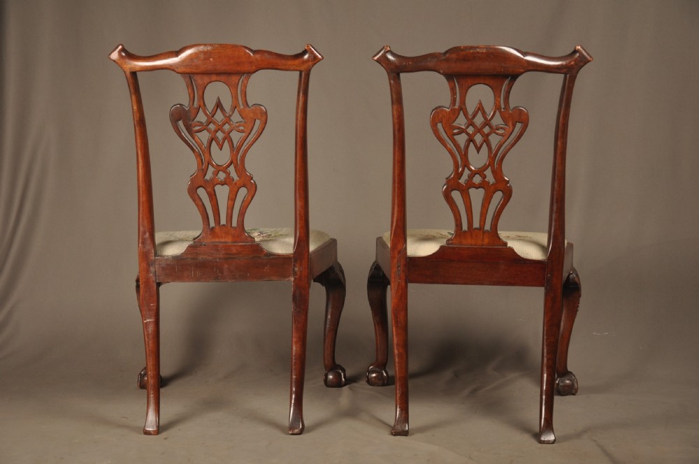 A pair of 18th-century George II mahogany side chairs featuring pierced carved splats, cabriole legs with claw and ball feet, and floral needlepoint drop-in seats. View X