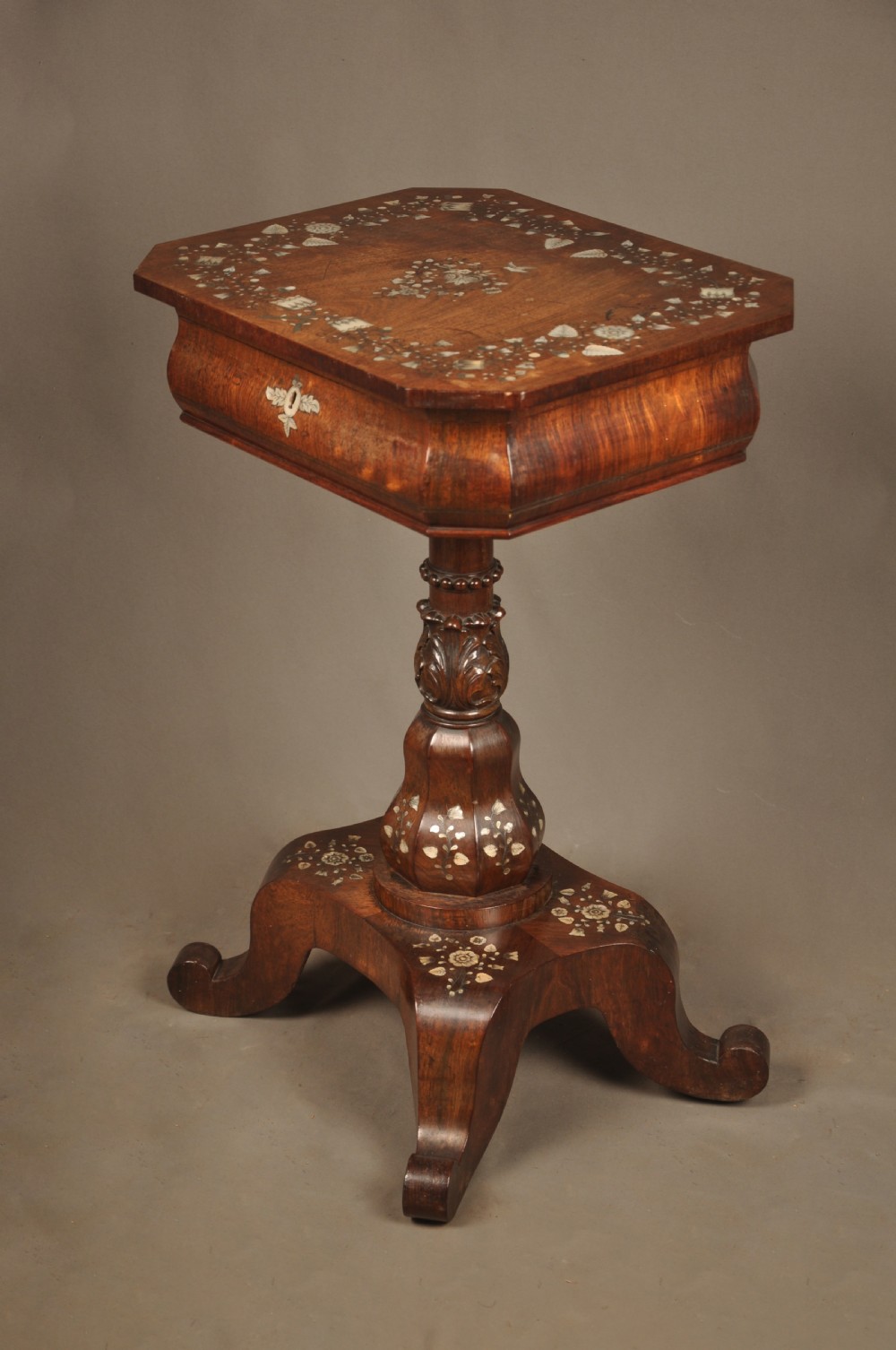 An antique octagonal mahogany work table with mother-of-pearl floral inlay, a central carved pedestal, and a quadruped base.