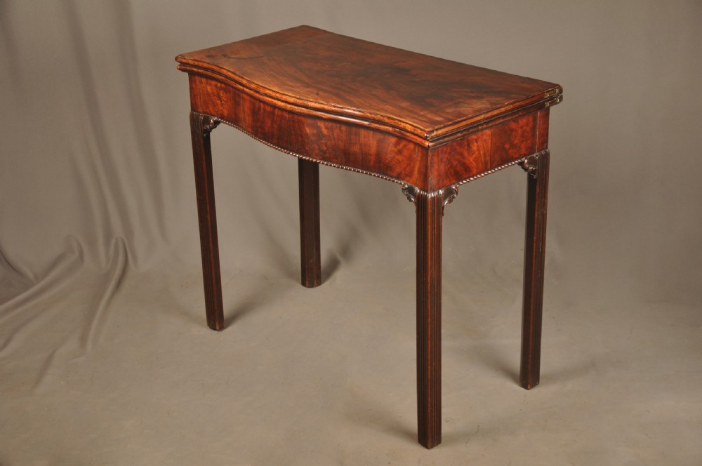 An 18th-century Georgian mahogany card table with a folded serpentine top and fluted legs.