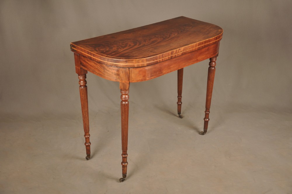 A late eighteenth-century mahogany fold-over card table featuring satinwood inlay, a reeded apron, and fluted legs on brass castors. View II