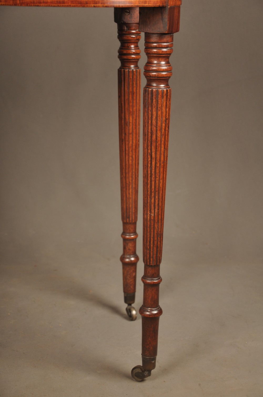 A late eighteenth-century mahogany fold-over card table featuring satinwood inlay, a reeded apron, and fluted legs on brass castors. View IV