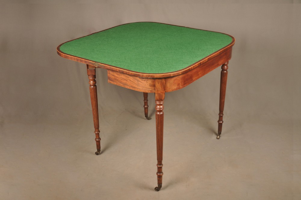 A late eighteenth-century mahogany fold-over card table featuring satinwood inlay, a reeded apron, and fluted legs on brass castors. View VII