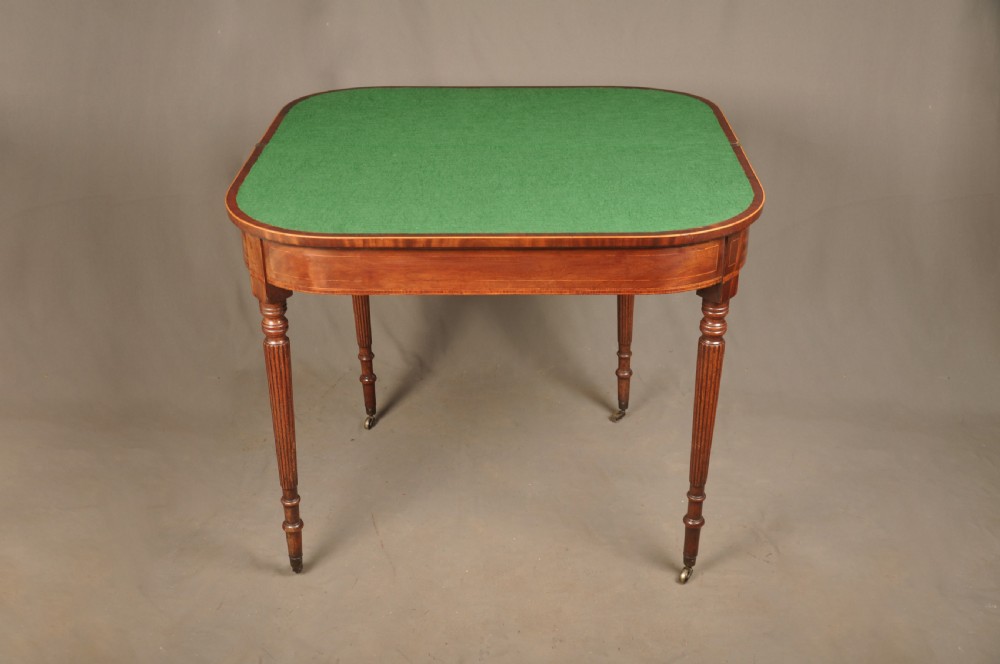 A late eighteenth-century mahogany fold-over card table featuring satinwood inlay, a reeded apron, and fluted legs on brass castors. View VIII
