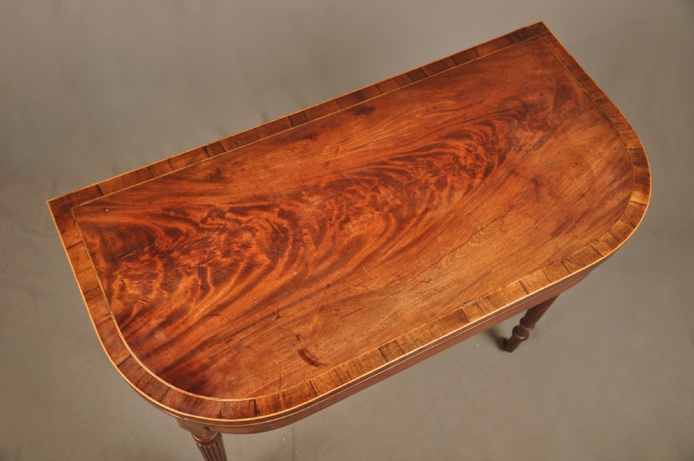 A late eighteenth-century mahogany fold-over card table featuring satinwood inlay, a reeded apron, and fluted legs on brass castors. View XI