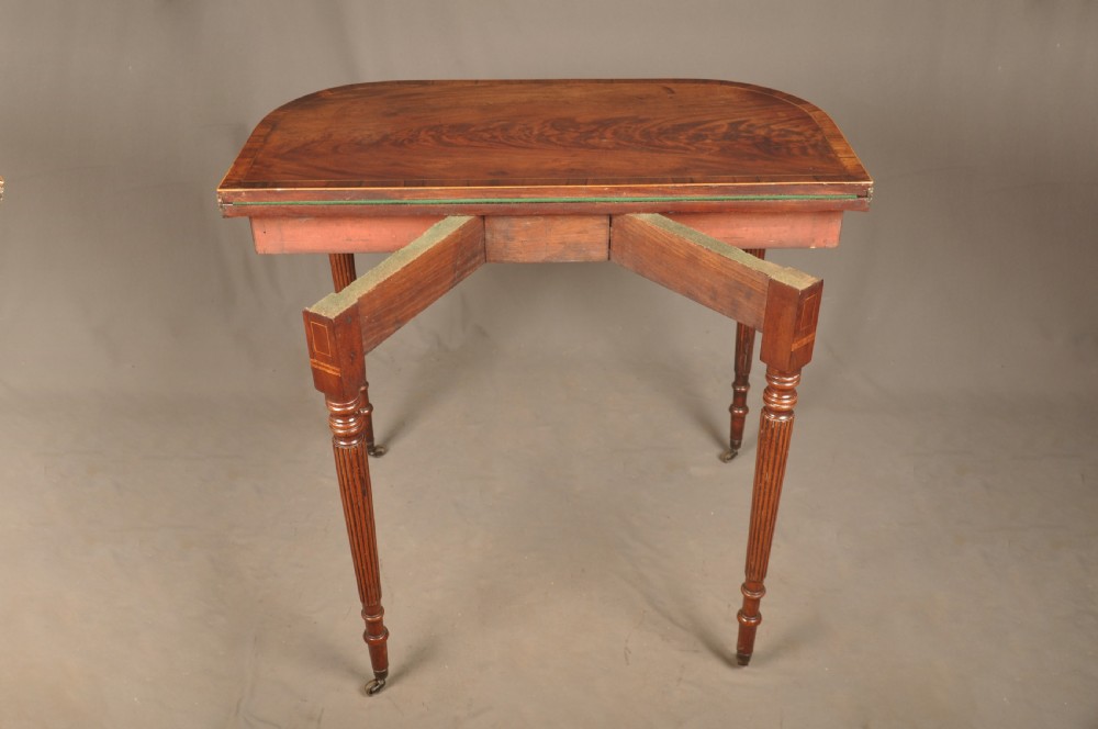 A late eighteenth-century mahogany fold-over card table featuring satinwood inlay, a reeded apron, and fluted legs on brass castors. View XIII