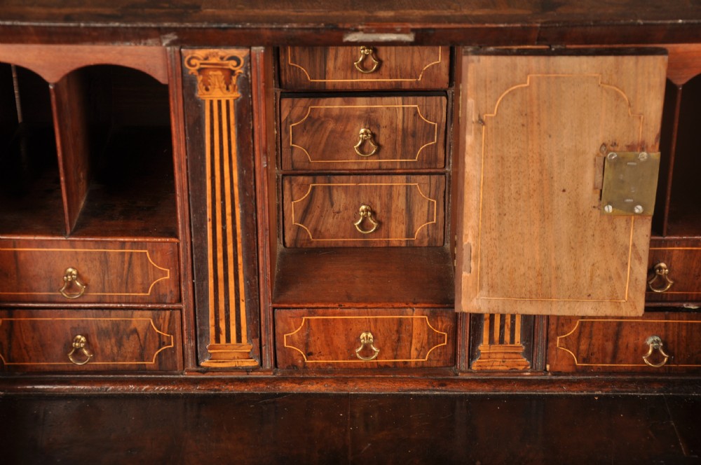 An early 18th-century Irish walnut slant-front bureau featuring engraved brass drop handles, keyhole escutcheons, and bracket feet. View V