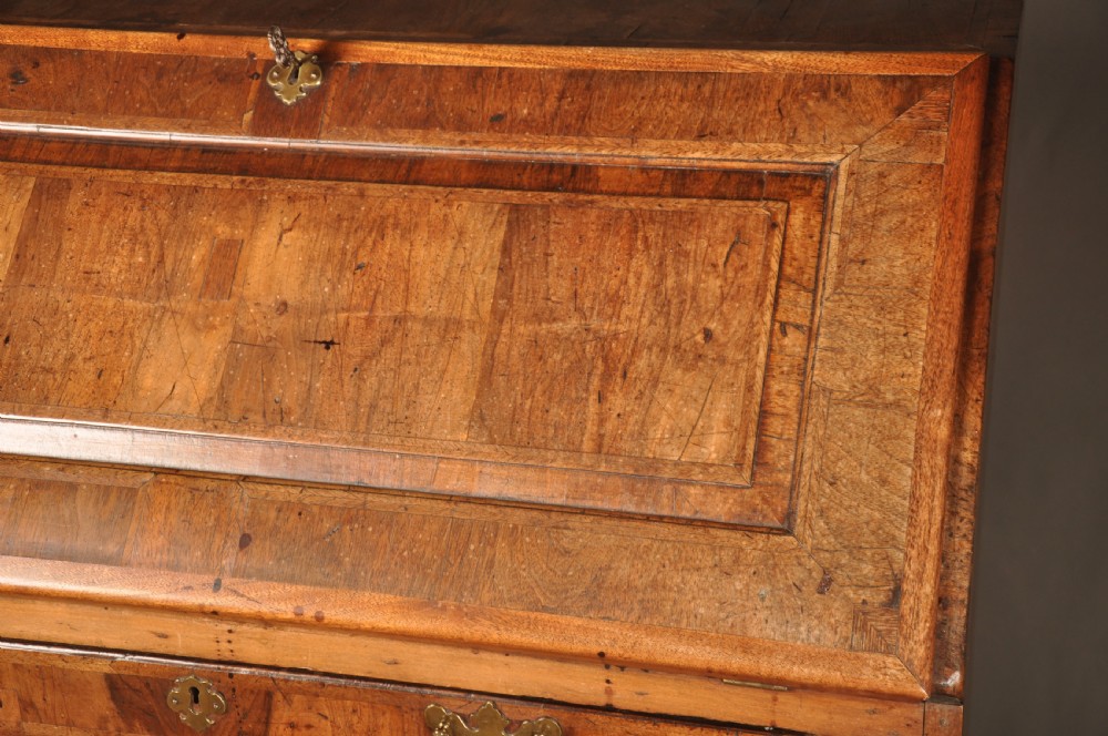 An early 18th-century Irish walnut slant-front bureau featuring engraved brass drop handles, keyhole escutcheons, and bracket feet. View IX
