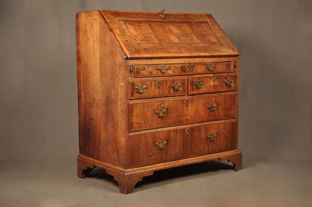 An early 18th-century Irish walnut slant-front bureau featuring engraved brass drop handles, keyhole escutcheons, and bracket feet. View X