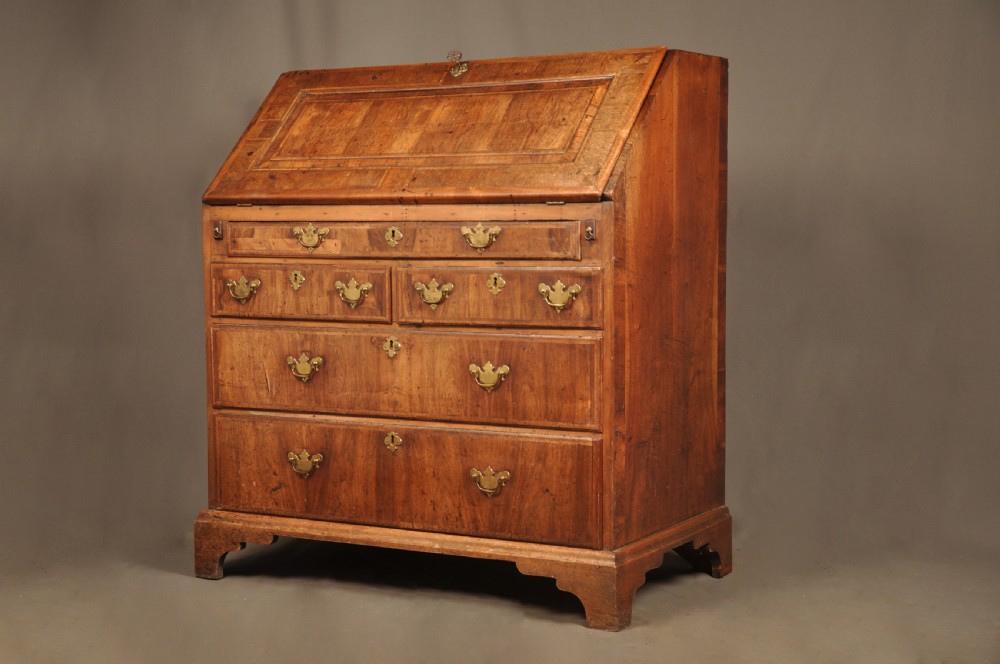 An early 18th-century Irish walnut slant-front bureau featuring engraved brass drop handles, keyhole escutcheons, and bracket feet. View XI