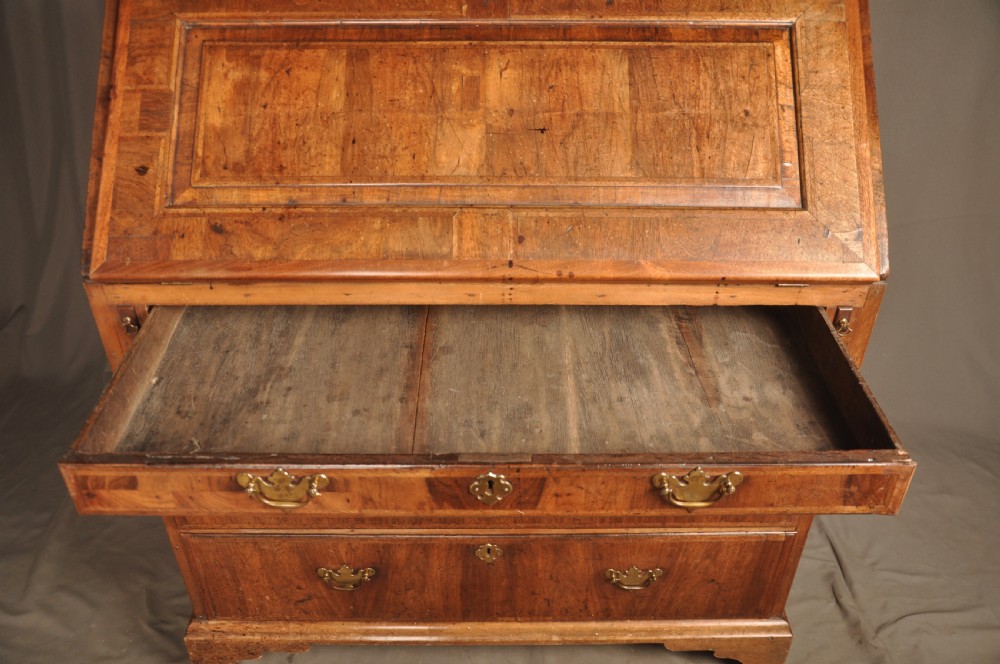 An early 18th-century Irish walnut slant-front bureau featuring engraved brass drop handles, keyhole escutcheons, and bracket feet. View XII
