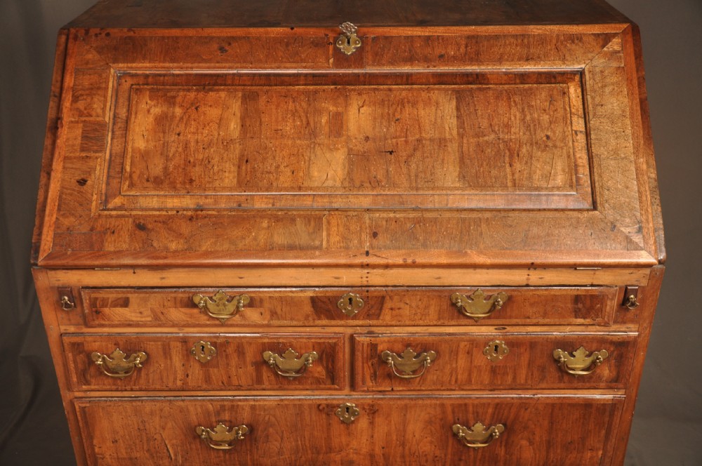 An early 18th-century Irish walnut slant-front bureau featuring engraved brass drop handles, keyhole escutcheons, and bracket feet. View XIV