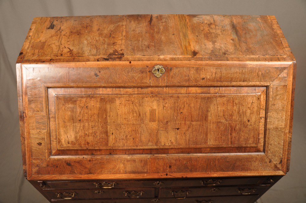 An early 18th-century Irish walnut slant-front bureau featuring engraved brass drop handles, keyhole escutcheons, and bracket feet. View XV