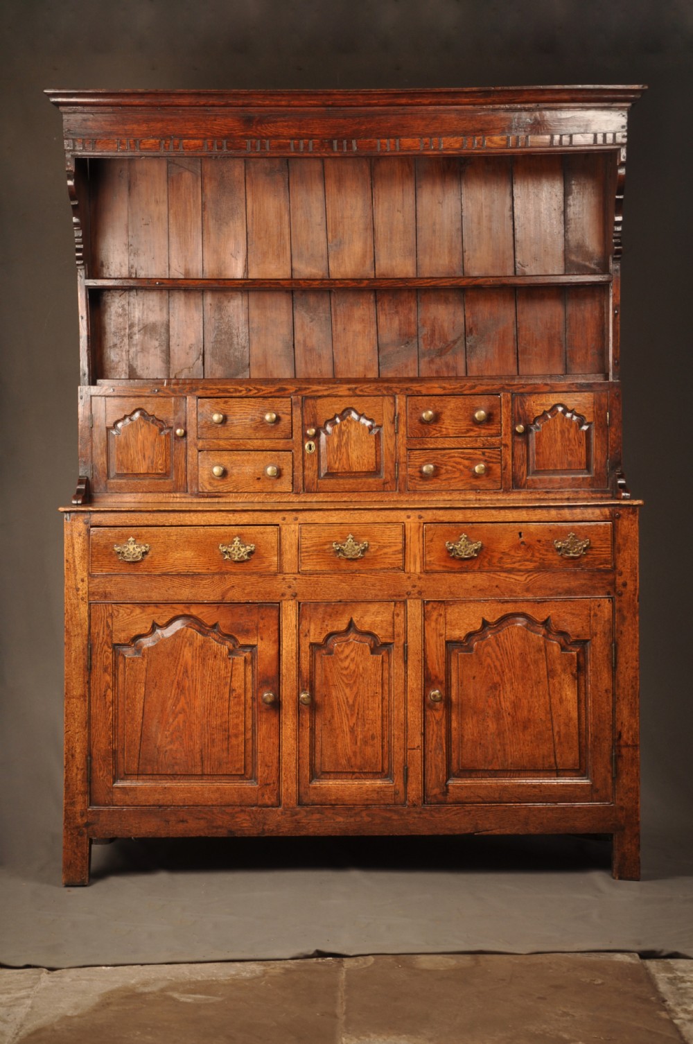 Mid 18th-century English oak dresser featuring an open tiered plate rack above small drawers, resting on a base with three drawers and three arched fielded panel cupboard doors.