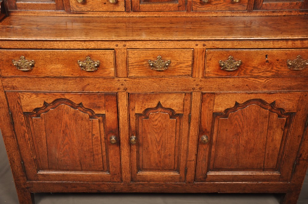 Mid 18th-century English oak dresser featuring an open tiered plate rack above small drawers, resting on a base with three drawers and three arched fielded panel cupboard doors. View IV