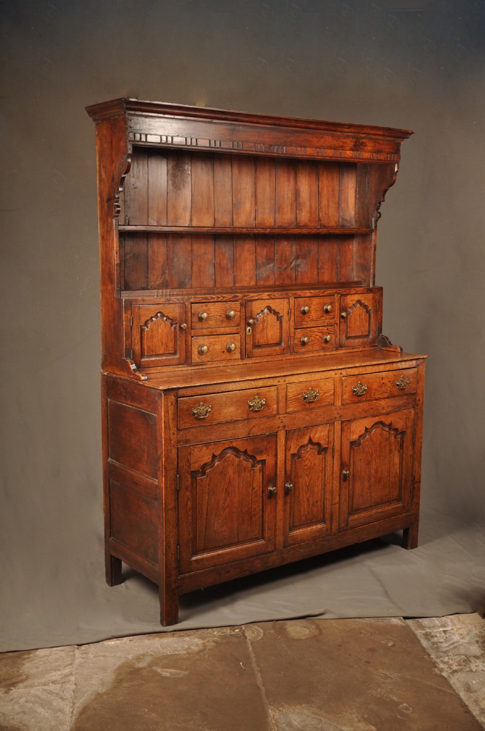 Mid 18th-century English oak dresser featuring an open tiered plate rack above small drawers, resting on a base with three drawers and three arched fielded panel cupboard doors. View V