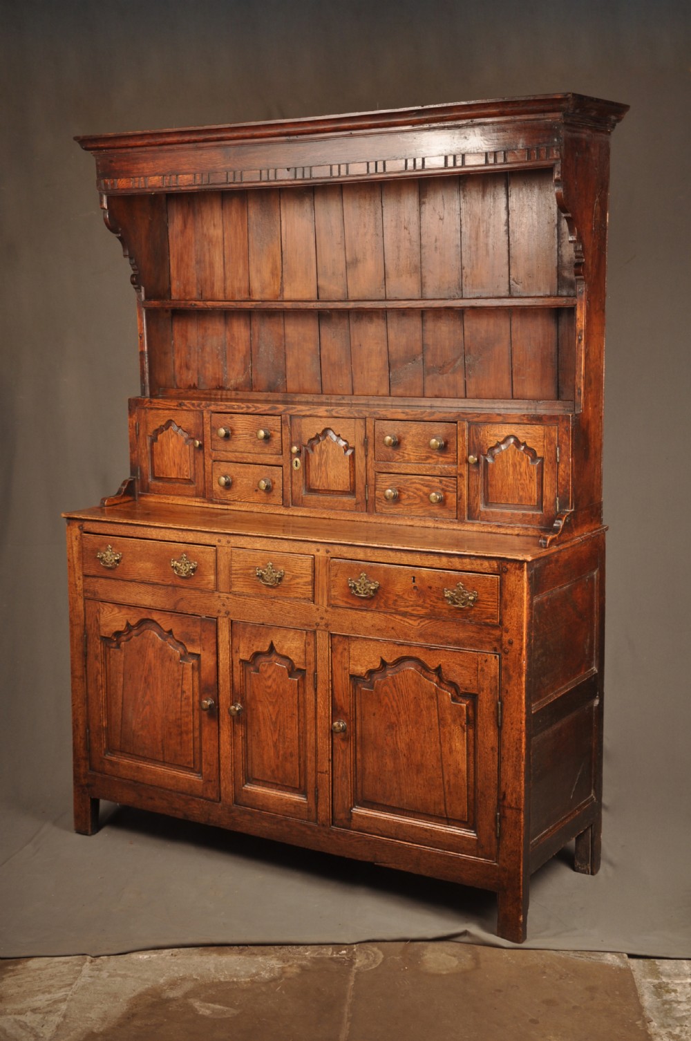 Mid 18th-century English oak dresser featuring an open tiered plate rack above small drawers, resting on a base with three drawers and three arched fielded panel cupboard doors. View VI