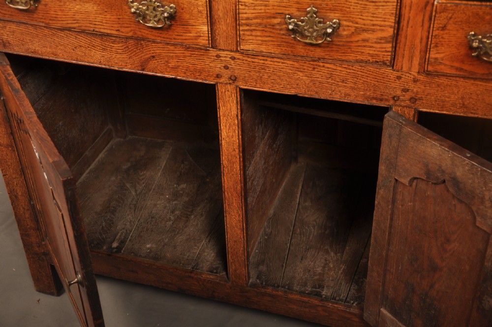 Mid 18th-century English oak dresser featuring an open tiered plate rack above small drawers, resting on a base with three drawers and three arched fielded panel cupboard doors. View VII