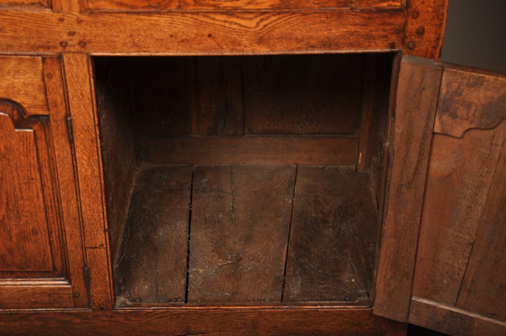 Mid 18th-century English oak dresser featuring an open tiered plate rack above small drawers, resting on a base with three drawers and three arched fielded panel cupboard doors. View VIII