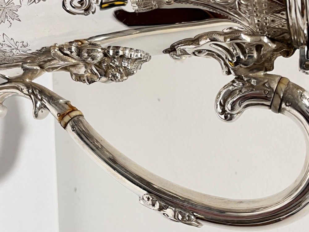 A Victorian lidded silver-plated jug featuring chased floral engraving, a scroll handle with insulating rings, and a hinged lid. View II
