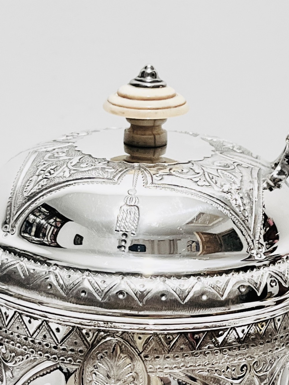 A Victorian lidded silver-plated jug featuring chased floral engraving, a scroll handle with insulating rings, and a hinged lid. View VI