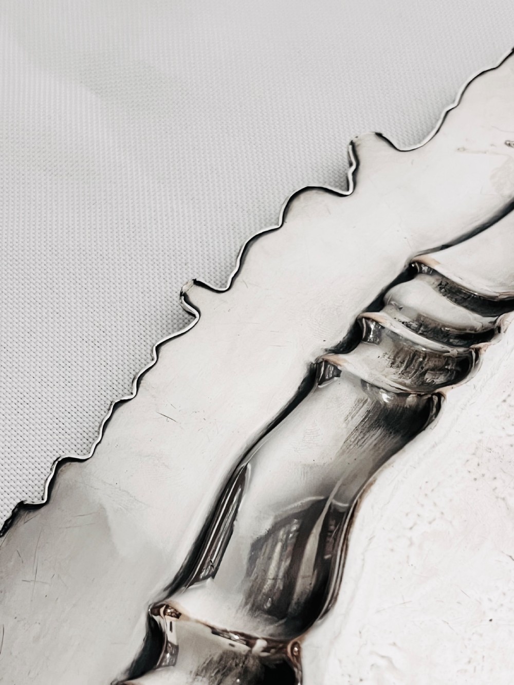 A circular silver plated salver featuring an ornate chased floral surface and a raised shell and scroll rim. View VII
