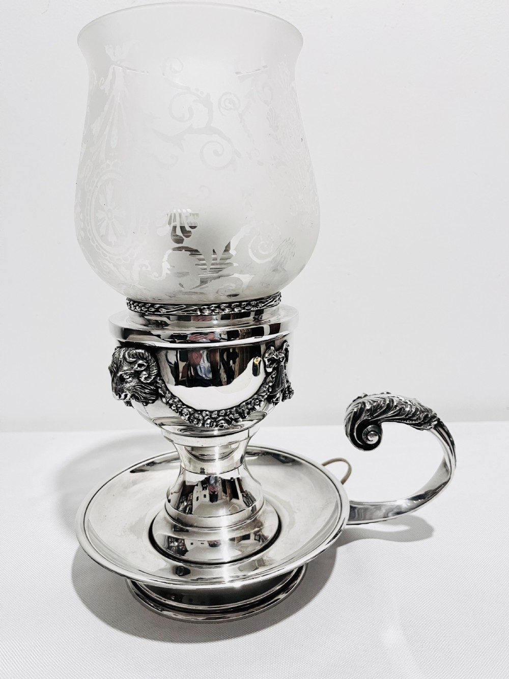 A late nineteenth-century German silver-plated chamberstick style table lamp with an etched frosted glass hurricane shade and a carved lion head motif.