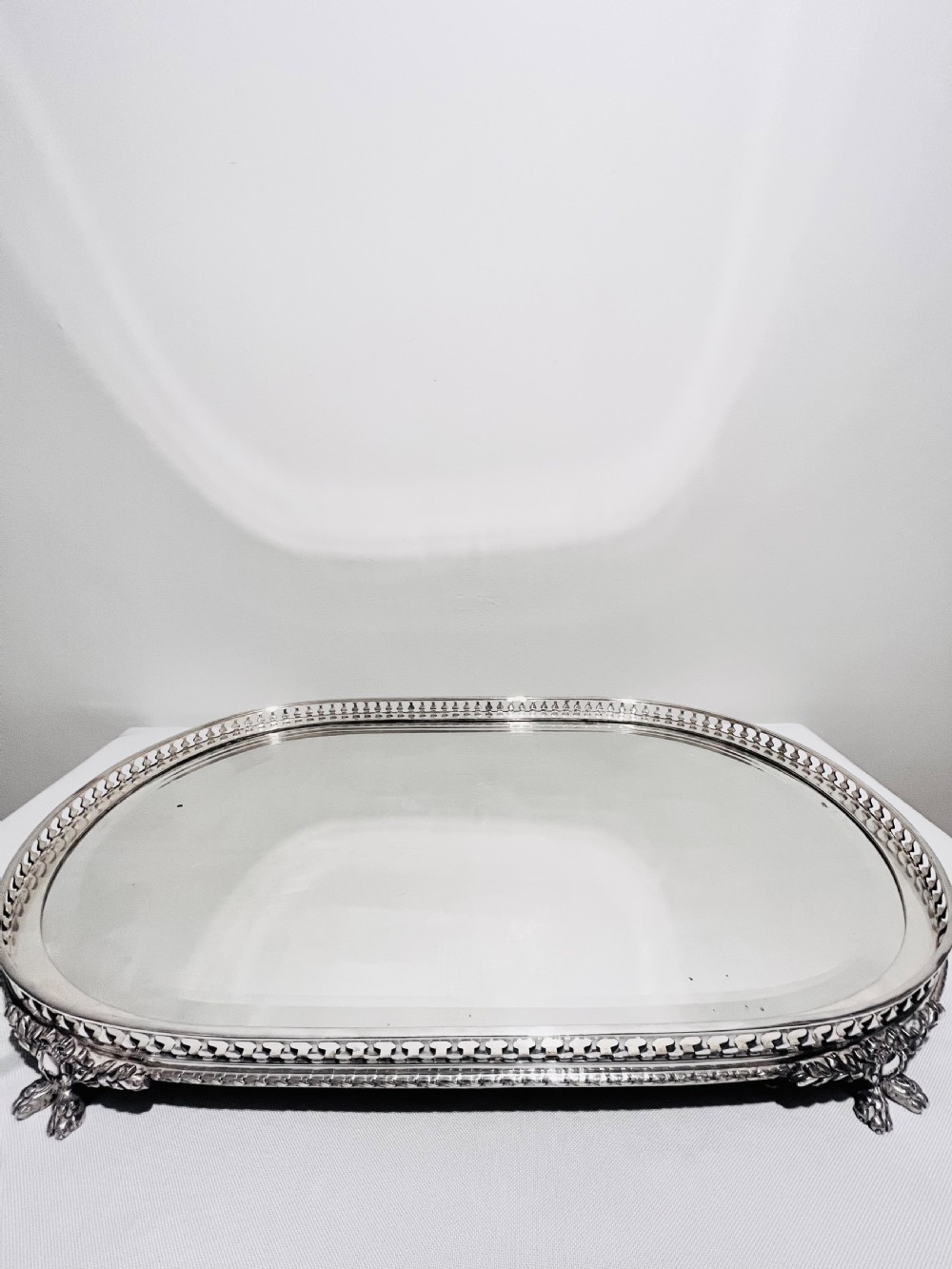 An antique late Victorian silver-plated table plateau featuring an oval mirrored surface enclosed by a pierced gallery rim and resting on cast feet.
