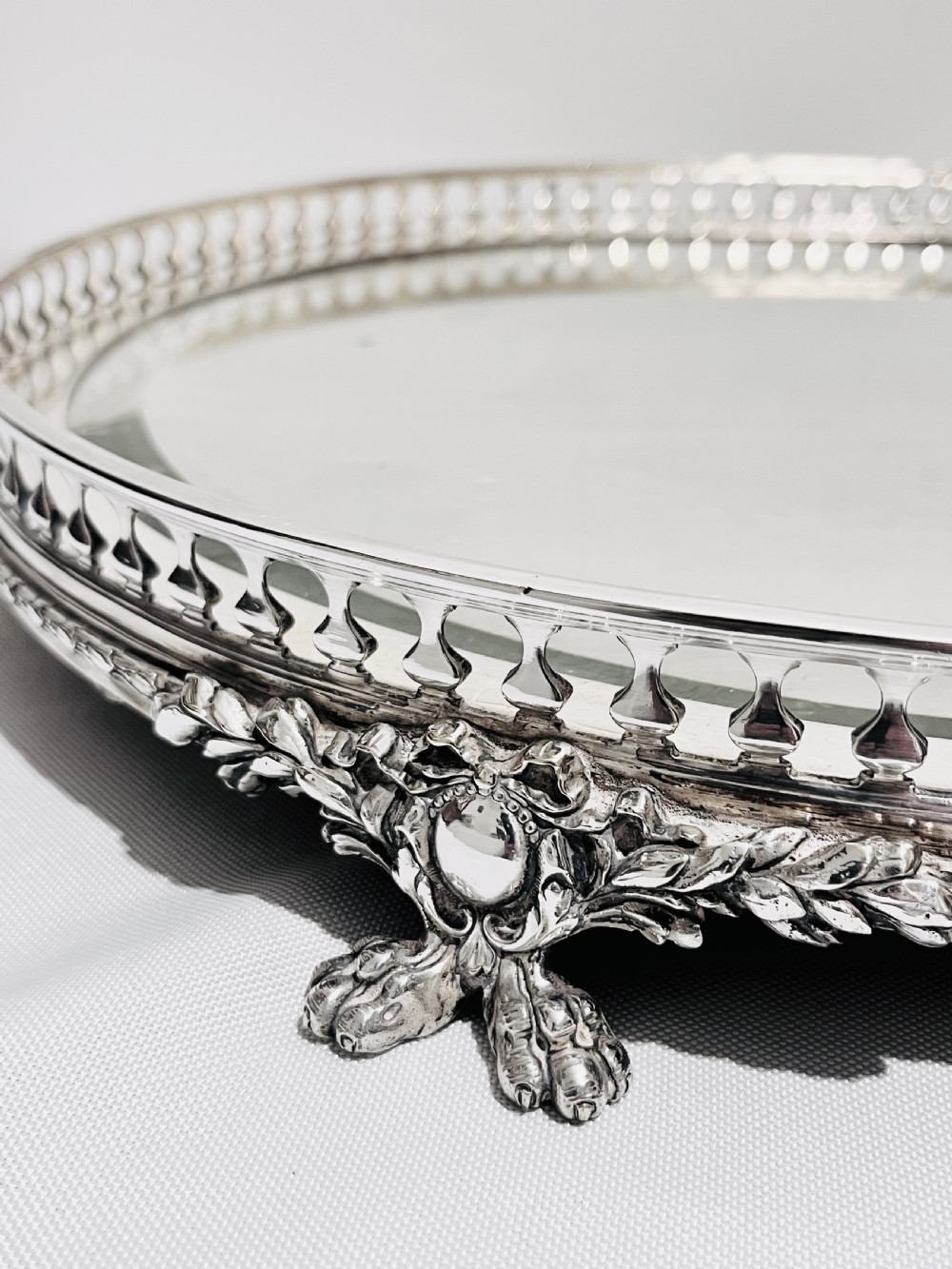 An antique late Victorian silver-plated table plateau featuring an oval mirrored surface enclosed by a pierced gallery rim and resting on cast feet. View II