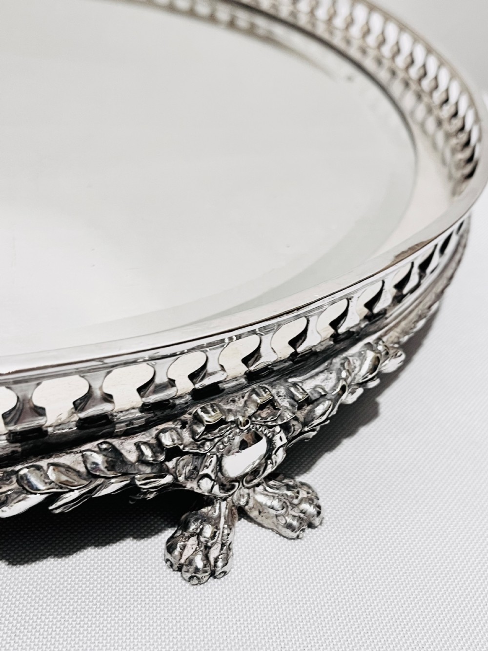 An antique late Victorian silver-plated table plateau featuring an oval mirrored surface enclosed by a pierced gallery rim and resting on cast feet. View III