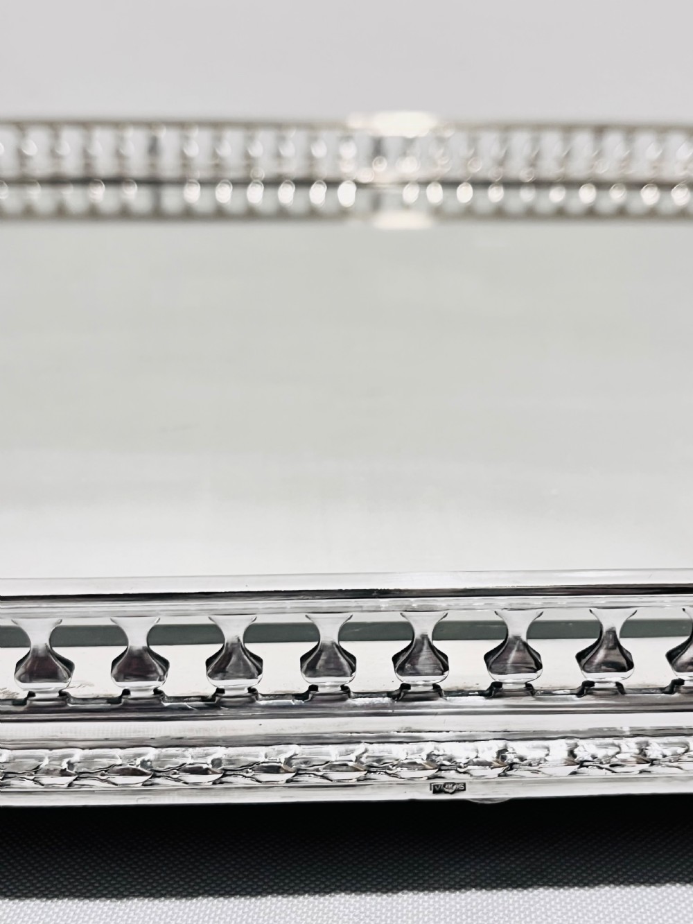 An antique late Victorian silver-plated table plateau featuring an oval mirrored surface enclosed by a pierced gallery rim and resting on cast feet. View V