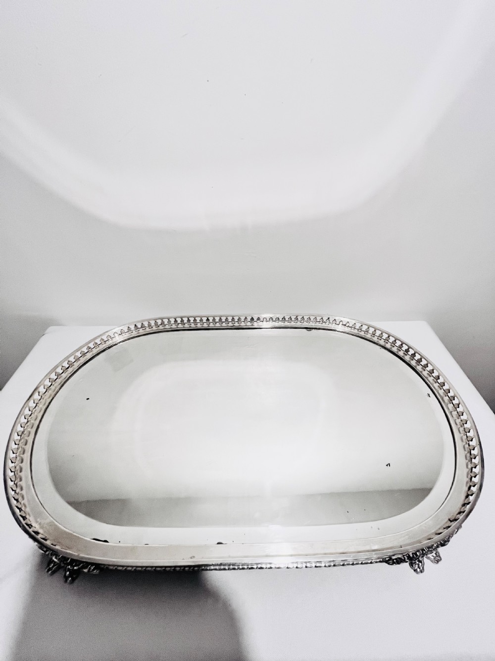 An antique late Victorian silver-plated table plateau featuring an oval mirrored surface enclosed by a pierced gallery rim and resting on cast feet. View VII