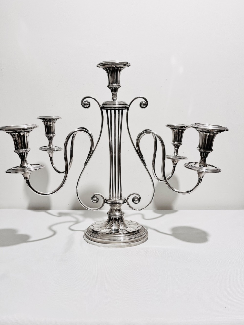 An antique silver-plated five-light candelabra featuring a central lyre-shaped stem with five scrolling branches terminating in circular candle nozzles.