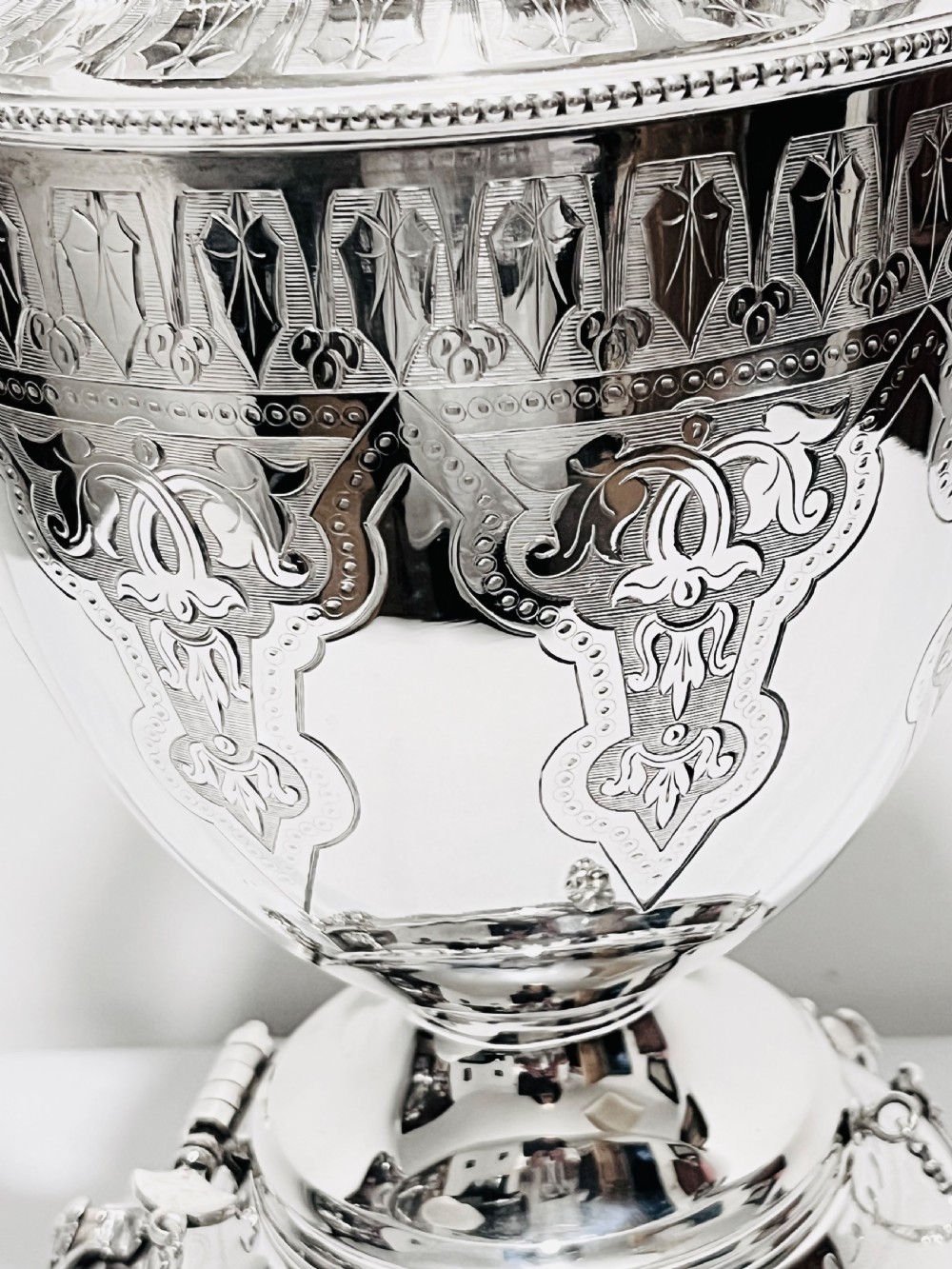 An ornate late Victorian silver-plated tea kettle with engraved geometric panels resting on a matching spirit burner stand. View IV