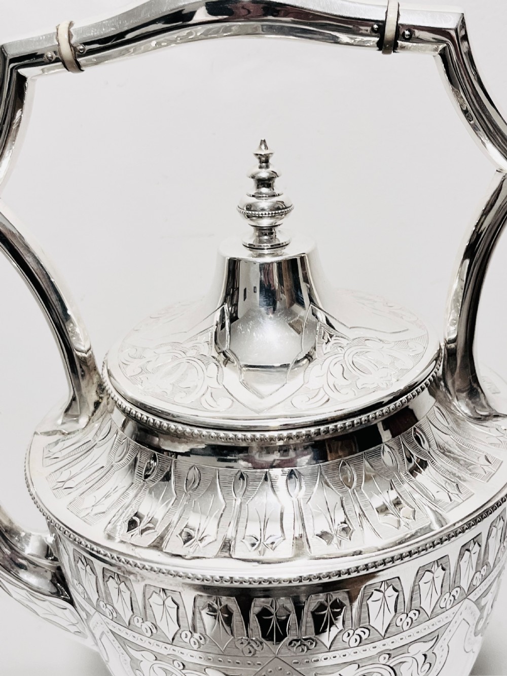 An ornate late Victorian silver-plated tea kettle with engraved geometric panels resting on a matching spirit burner stand. View VI