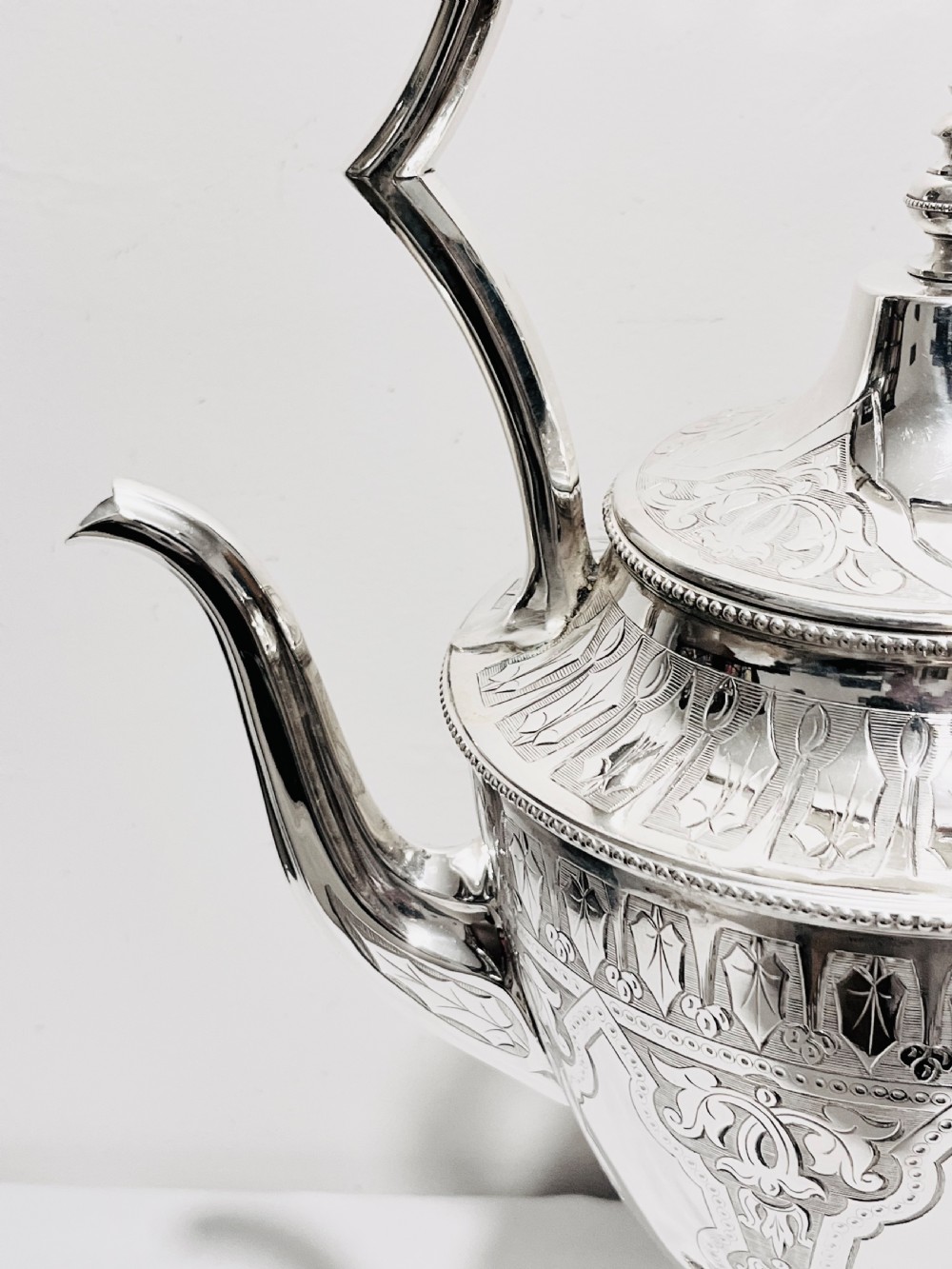 An ornate late Victorian silver-plated tea kettle with engraved geometric panels resting on a matching spirit burner stand. View VII