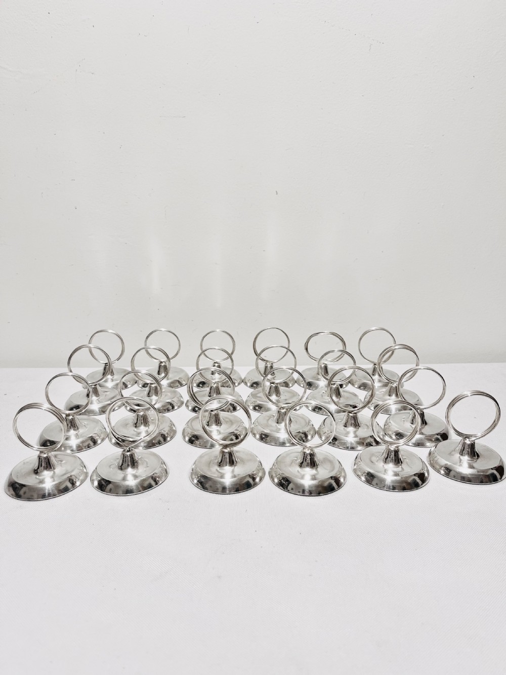 A collection of twenty-four silver-plated menu holders featuring domed bases and circular clip rings.